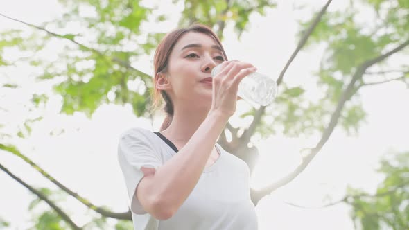 Asian woman take a break, drinking water from bottle after exercise.