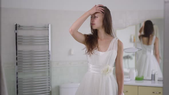 Happy Gorgeous Slim Woman in White Wedding Dress Standing in Bathroom at Home Looking Away