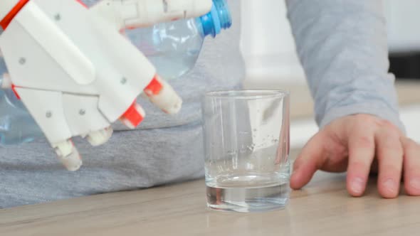 Man with Robotic Prosthetic Hand Is Pouring Water in Glass From the Bottle and Drinking It in the