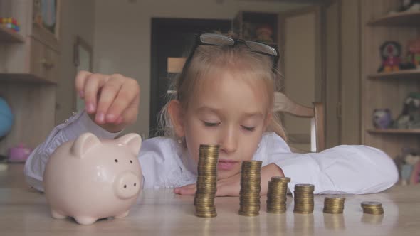 Happy Girl Save Money in Piggy Bank in Her Home. Child Inserting a Coin Into a Piggy Bank, Indoor