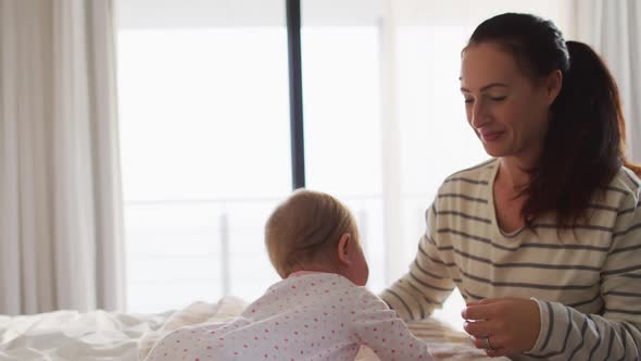 Caucasian mother smiling while playing with her baby on the bed at home