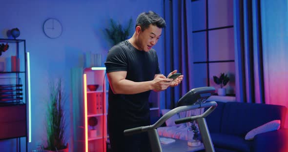 Asian Man in Sportswear Recieving Good news on Smartphone During Exercising