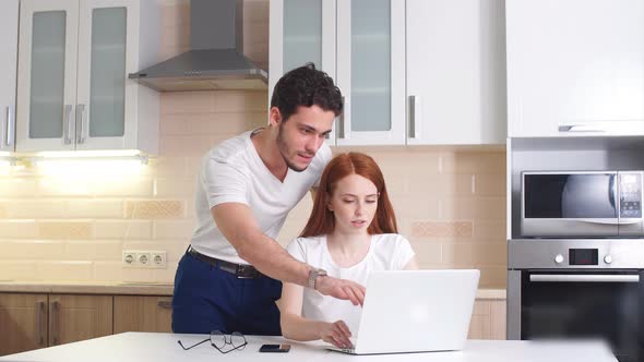 Young Business Couple Talking and Using Tablet in Kitchen at Home