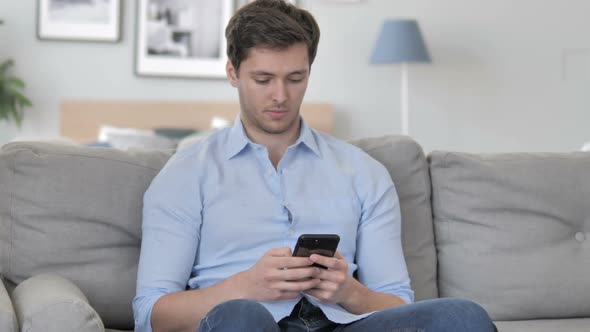 Young Man Using Smartphone While Relaxing on Sofa