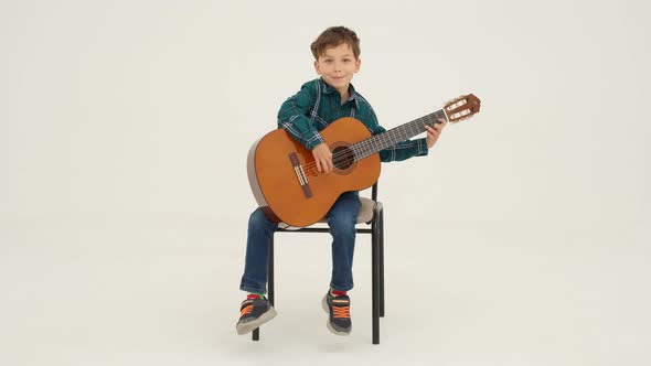 Little Boy is Playing Big Classical Guitar Sitting on the Stool