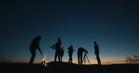 Friends with Campfire Looking Through Telescope in Night