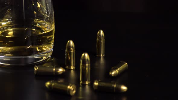 Closeup on a Glass of Whiskey and Bullets on a Black Table