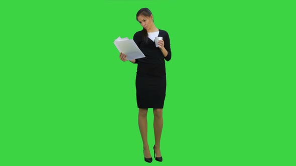 Young Businesswoman Reading Documents While Drinking Coffee on a Green Screen, Chroma Key