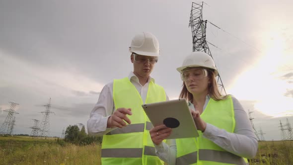 An Electrician Male and Female in the Fields Near the Power Transmission Line