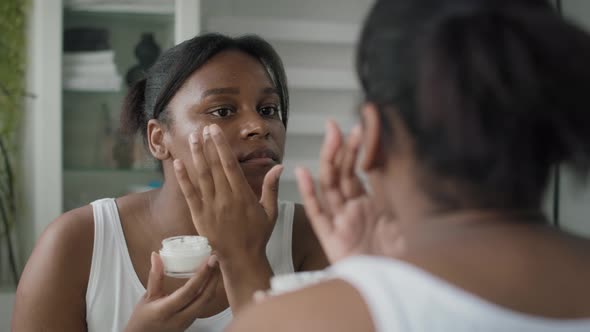 Young African-American  woman applying face cream in the mirror reflection. Shot with RED helium cam