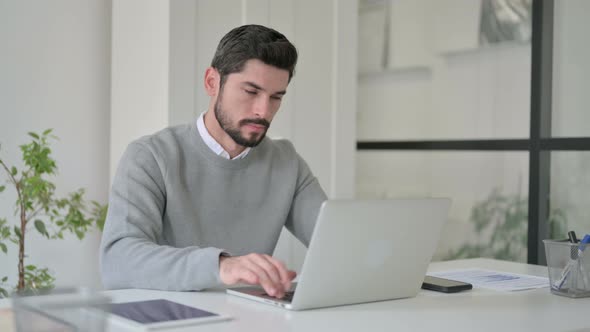 Young Man Showing Thumbs Up Sign While Using Laptop at Work