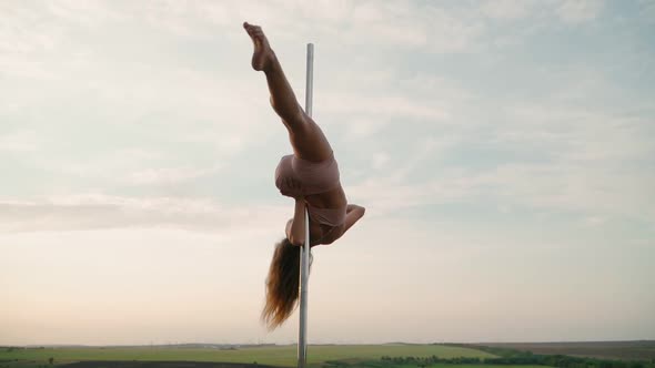 Beautiful Athletic Woman Performs Tricks on the Pole Against the Background of Sunset in the Field