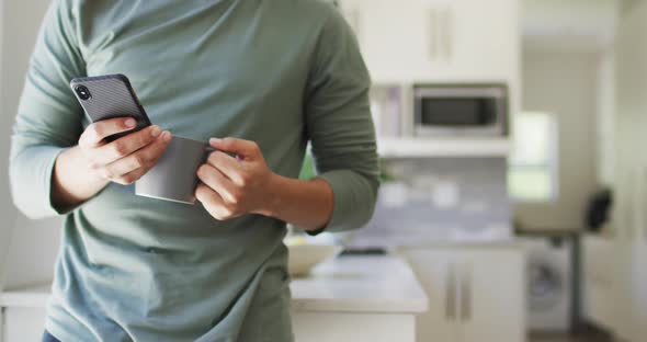 Mid section of biracial man using smartphone and drinking coffee in garden