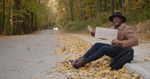 Black Hitchhiker with a Sign in Hands on the Roadside