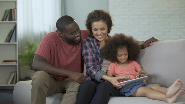 Parents watching their little daughter coping with educational app on tablet