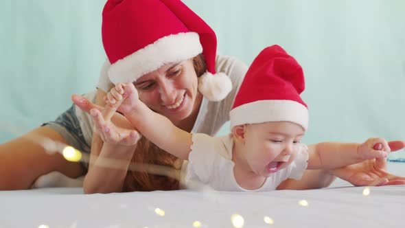 Mother Playing with Her Adorable Baby on the Bed at Home. Lots of Christmas Decorations Around Them