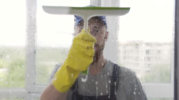 Focused Young Male Washer Wipping the Wet Window with a Little Mop