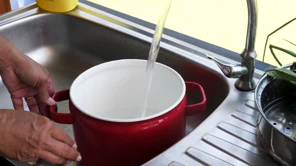 Chef turns on faucet and fills up red cooking pot with water for boiling