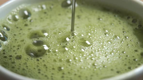 Matcha green tea frothing with frother in slow motion with a bubble swirl