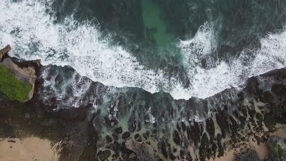 Top down aerial view of giant ocean waves crashing and foaming in coral beach