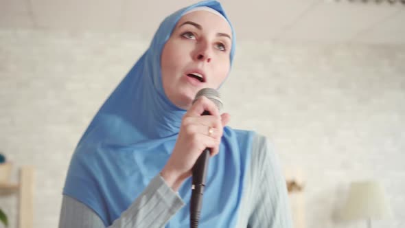 Portrait of Cheerful Expressive Muslim Girl in Hijab in Karaoke Microphone at Home
