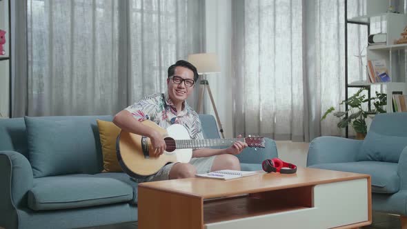 Man Composer With Notebook On Table Wearing Headphones And Smiling To Camera While Playing Guitar