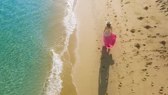 Happy Woman in Pink Beach Dress Walking By Scenic Tropical Ocean Beach at Sunset