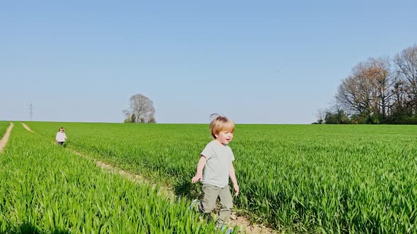 Two Little Kids Girl and a Boy Run in Green Spring Field