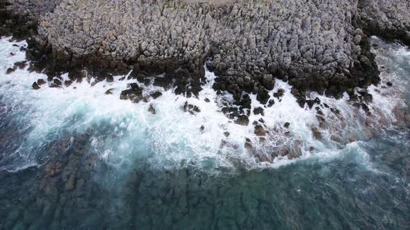Aerial top view 4k footage by drone of ocean blue waves break on the high cliff of a rocky mountain