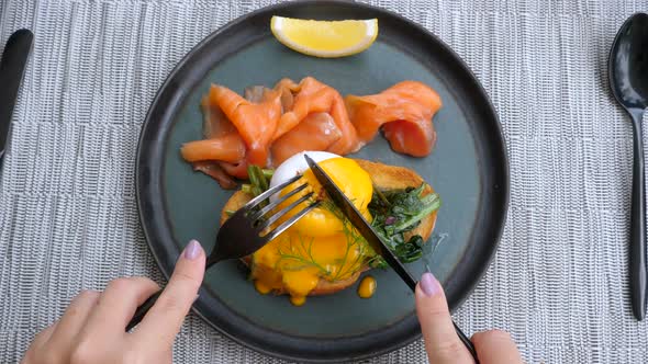 Top View of Woman Hands Cutting Poached Egg with Smoked Fish in Restaurant