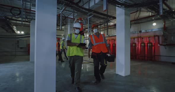 Engineers in Masks Examining Metal Structures in Workshop