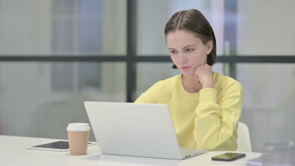Young Woman Thinking While Working on Laptop in Office