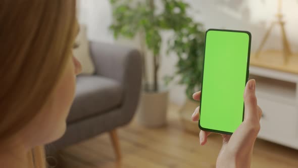 Back View of Woman at Living Room Using Phone With Green Mockup Screen Chroma Key Without Track