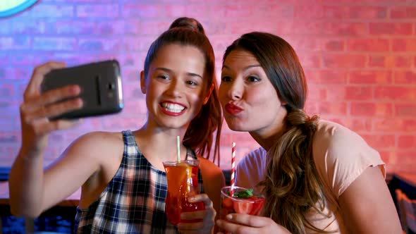 Friends taking selfie on mobile phone while having cocktail