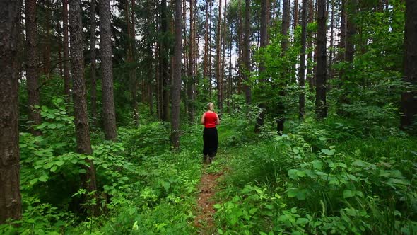 Woman in red top walking through woods in Poprad Slovakia. Dense forest with vibrant green foliage.