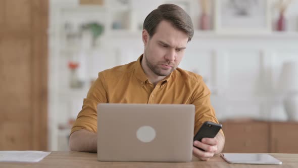 Young Man using Smartphone while using Laptop in Office