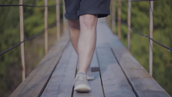 Guy Walks on Suspended Bridge in the Forest