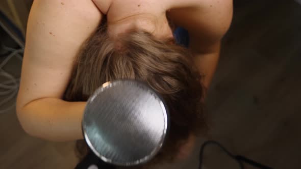 View from above a woman bent over with a hair dryer drying her fluffy hair