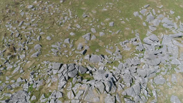 Top down aerial tracking forwards over a rocky outcrop with large boulders surrounded by grassy moor