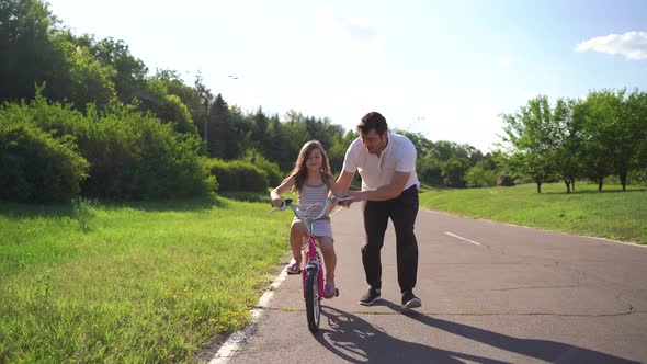 Young Father Teaching His Daughter to Ride Bicycle Outdoors