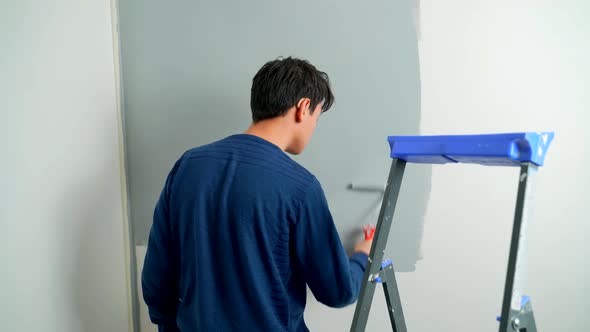 A Hearing-impaired Young Man in Hearing Aids Paints the Wall with a Roller Gray.