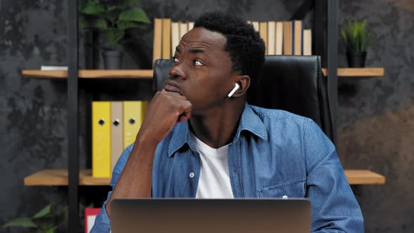 Thoughtful African American Man Sits on Chair at Table Works Laptop in Office