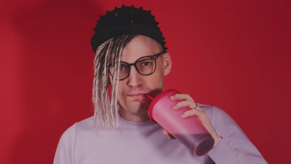 Young Handsome Stylish Man in Glasses Black Cap Drinking Refreshing Beverage on Red Background