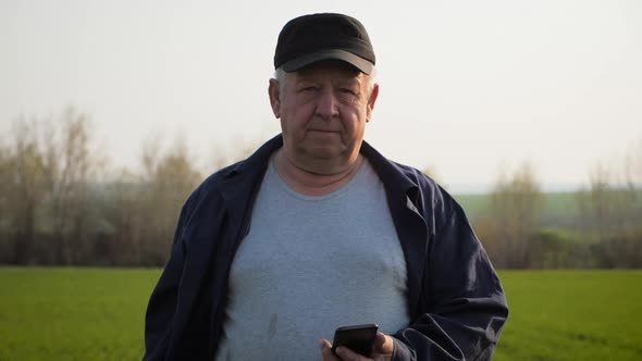 Mature Farmer Examining Soil and Using Smartphone Checking Report of Agriculture in a Field.