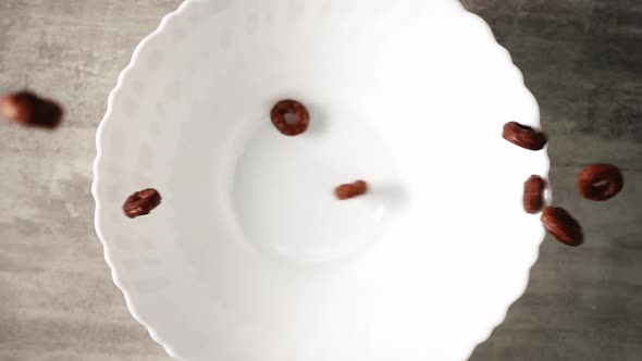 Chocolate Cornflakes in Form of Rings are Pouring in Slow Motion Into White Plate