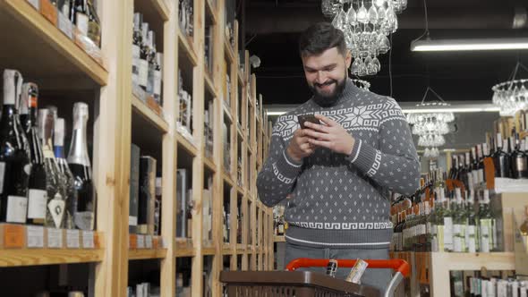 Handsome Man Using His Smart Phone While Shopping at Wine Store
