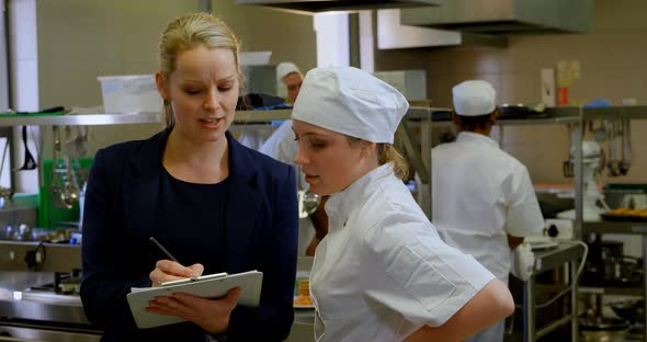 Female manager and female chefs discussing over clipboard 4k