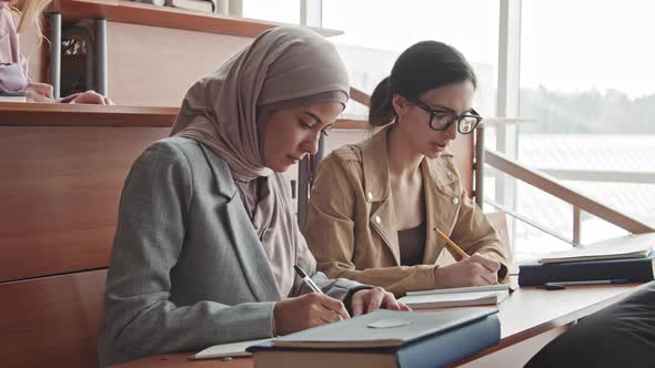 Two Female Students Taking Notes in Copybooks during Lecture