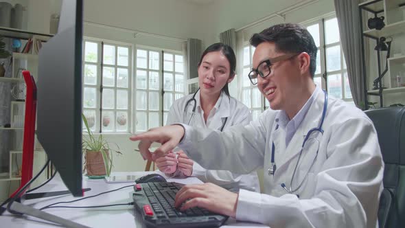 Two Asian Professional Physicians Talking, Consulting And Working On Computer