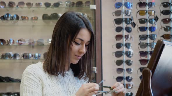 Cheerful Young Caucasian Woman in a Cozy White Sweater Trying on Transparent Glasses Near a Vintage